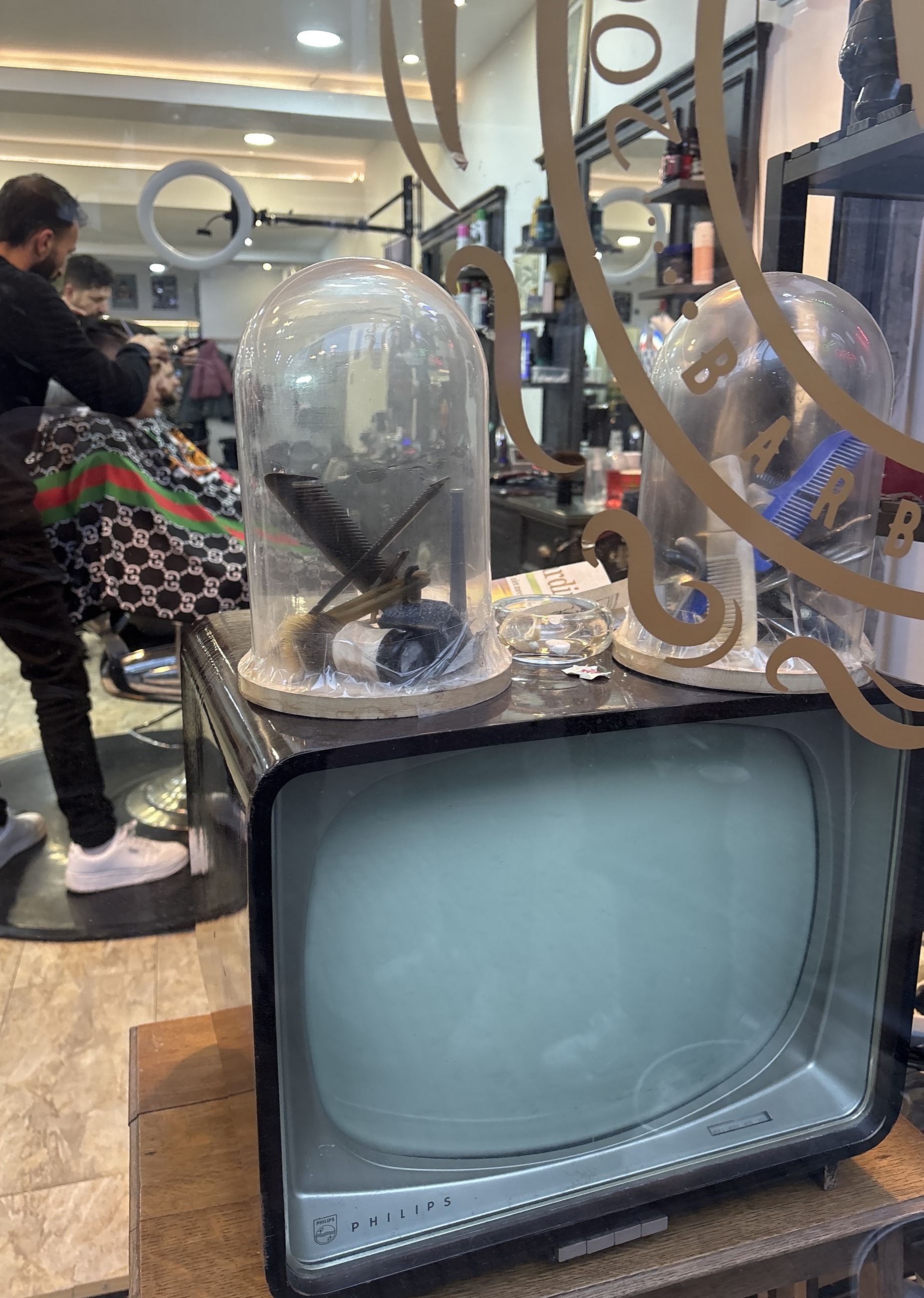 Een oude televisie met glazen stolpen erop, achter het raam met gouden belettering