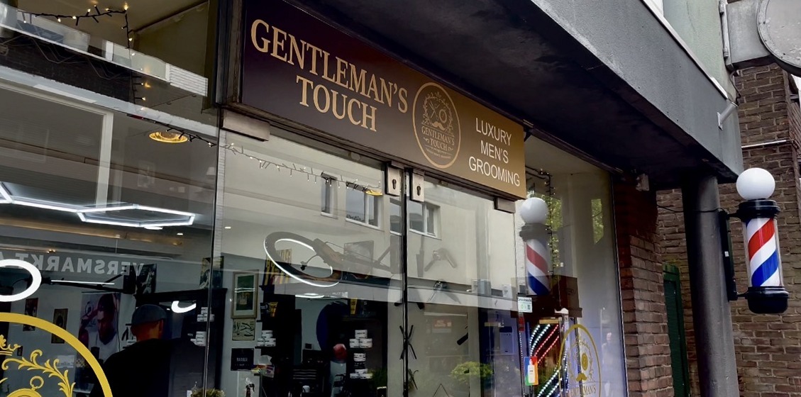 De gevel van Gentleman’s touch: bruin bord met gouden letters en een barberpaal naast het raam